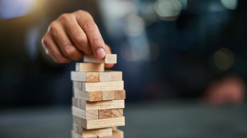 Hand placing wooden block atop a tower of blocks on a table