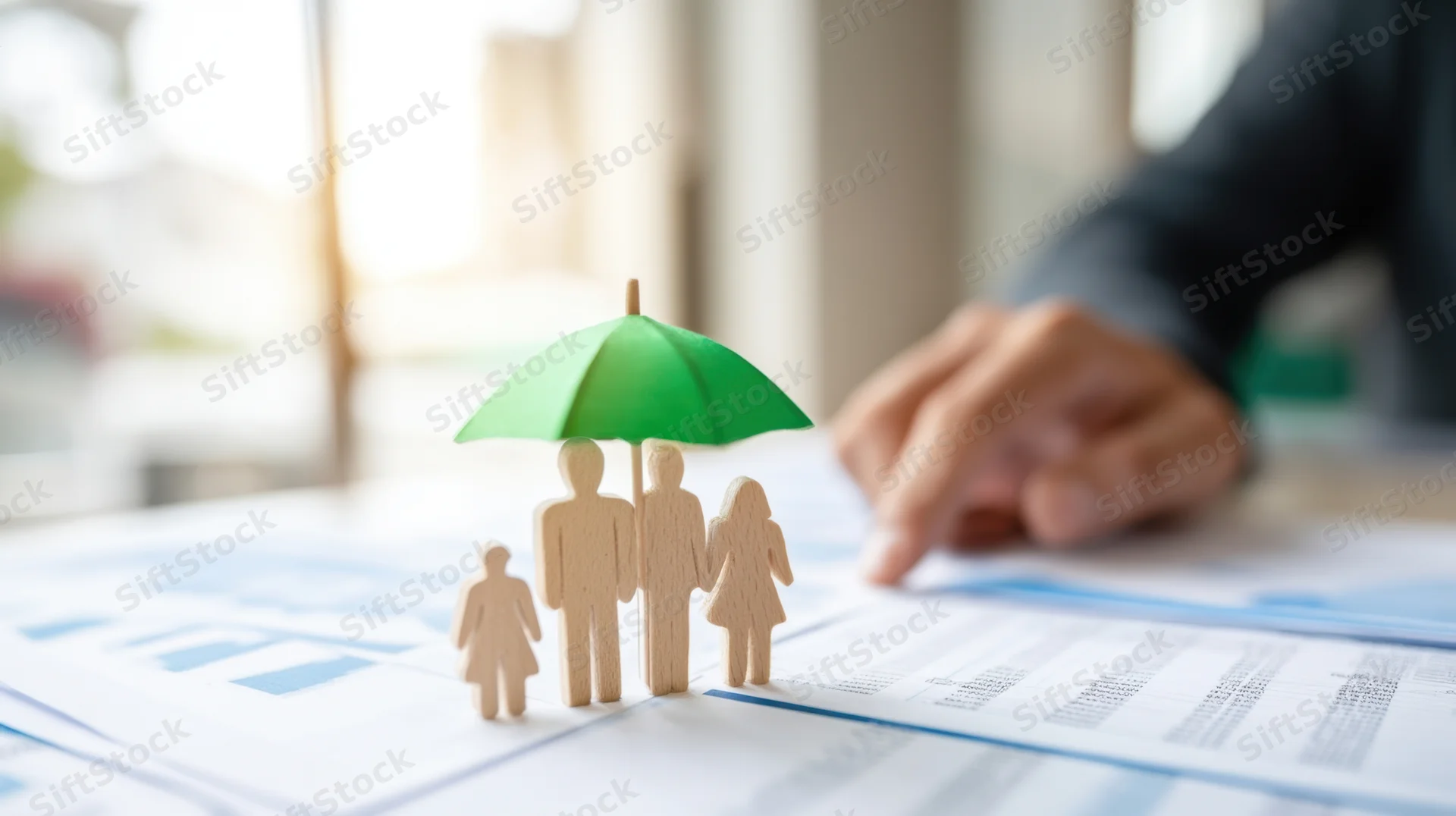 Wooden family figures under green umbrella on documents with hand pointing in office
