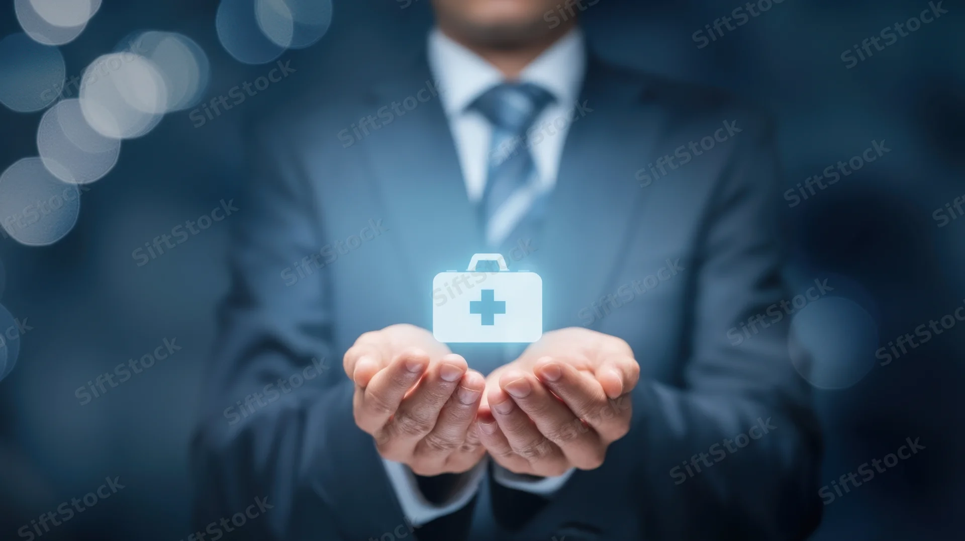 Businessman in suit holding glowing medical briefcase icon in hands against dark background with bokeh lights