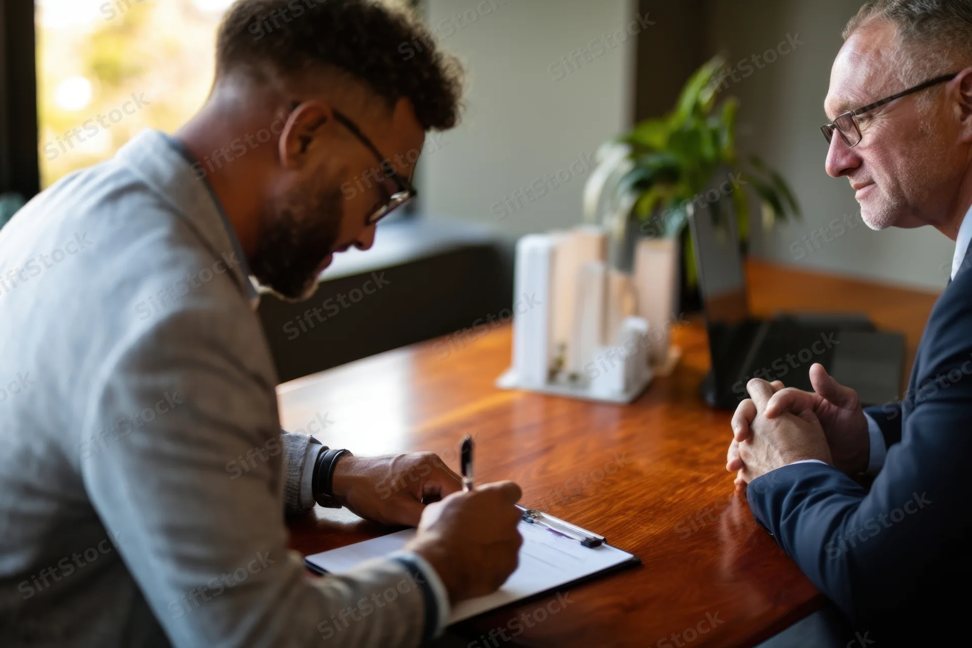 Two men in a business meeting signing a document at a wooden desk in an office