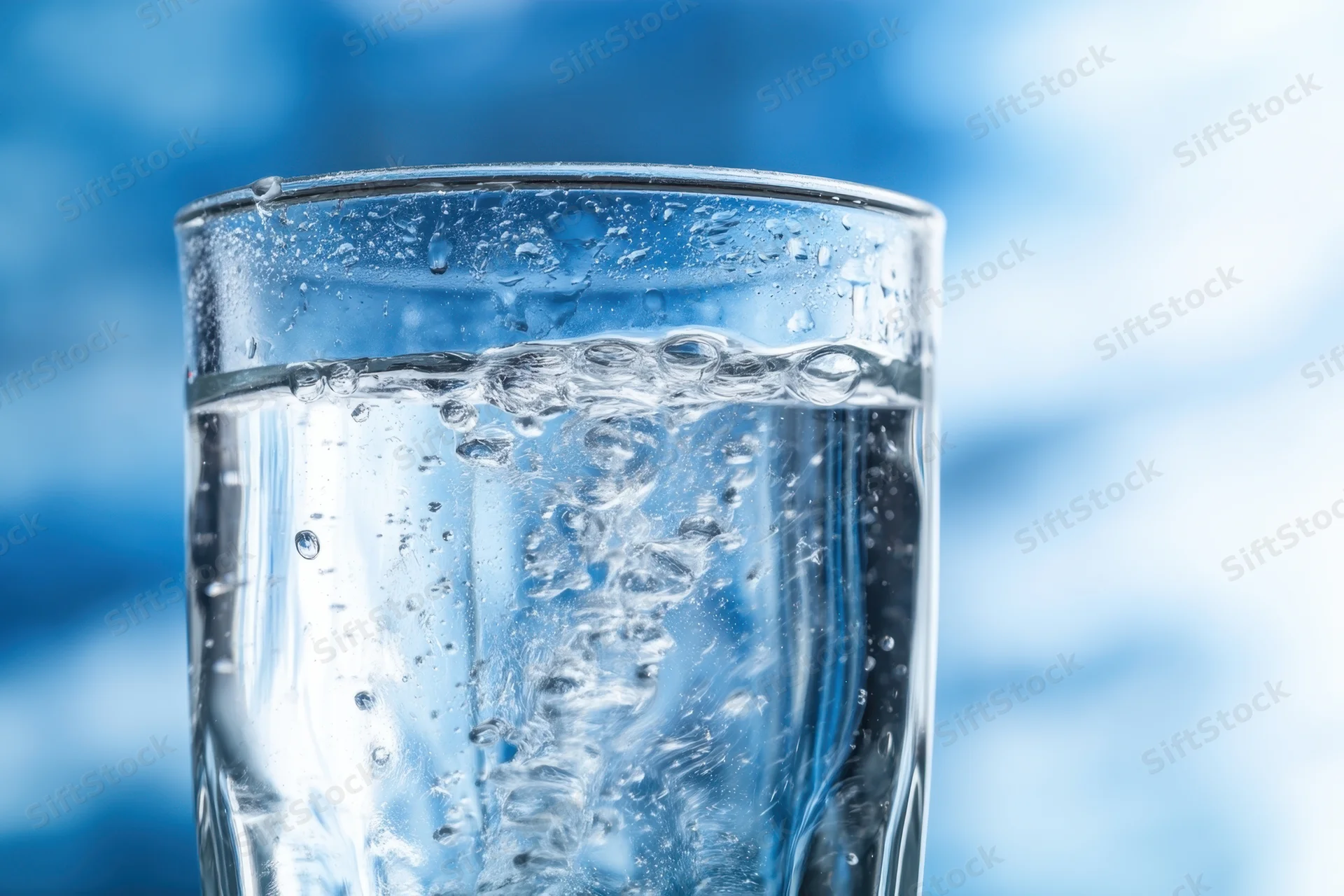 Closeup of a clear glass filled with cold sparkling water showing bubbles and condensation against a blue blurred background