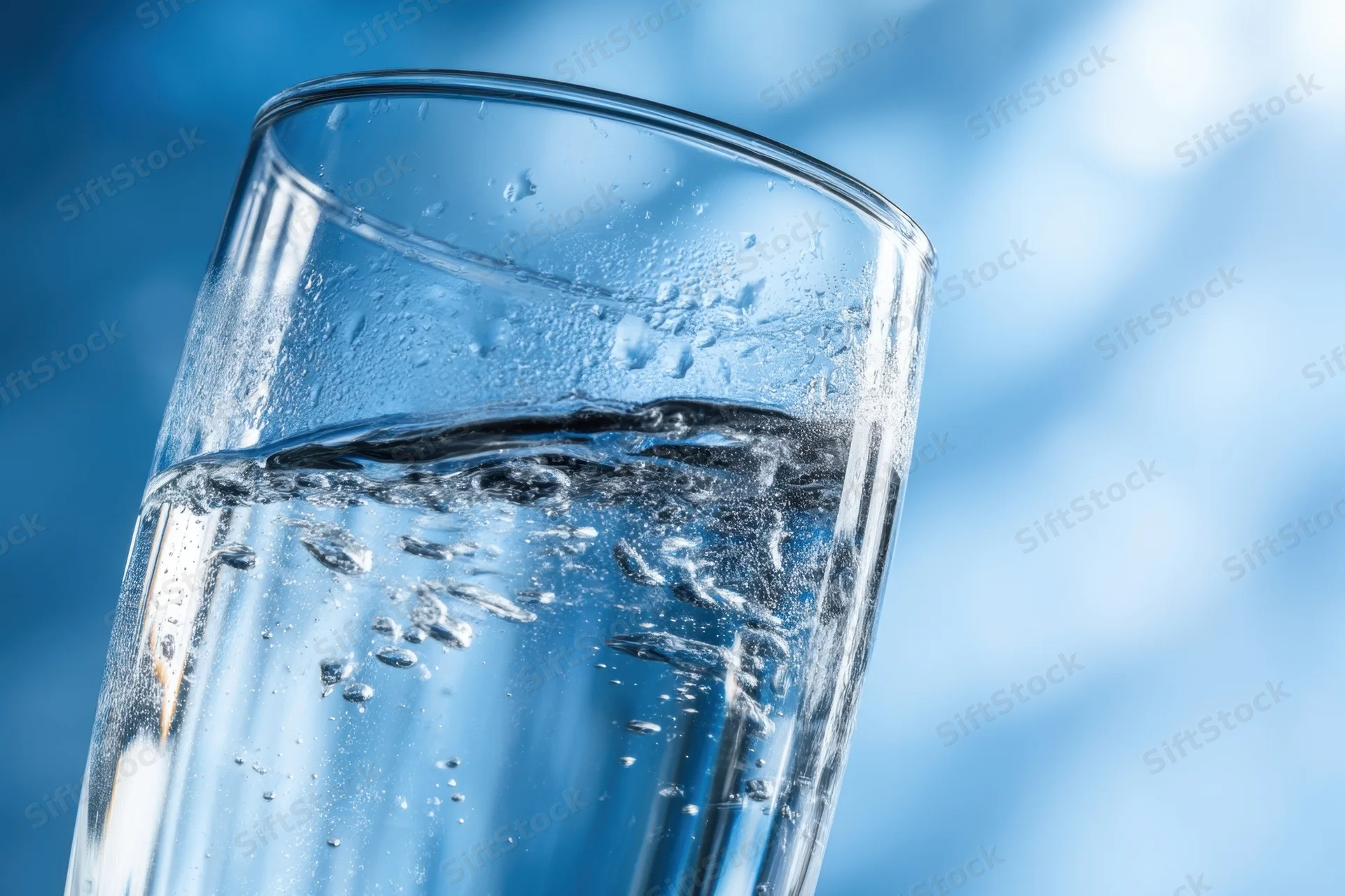 Closeup of a glass filled with cold water showing condensation and bubbles against a blue background