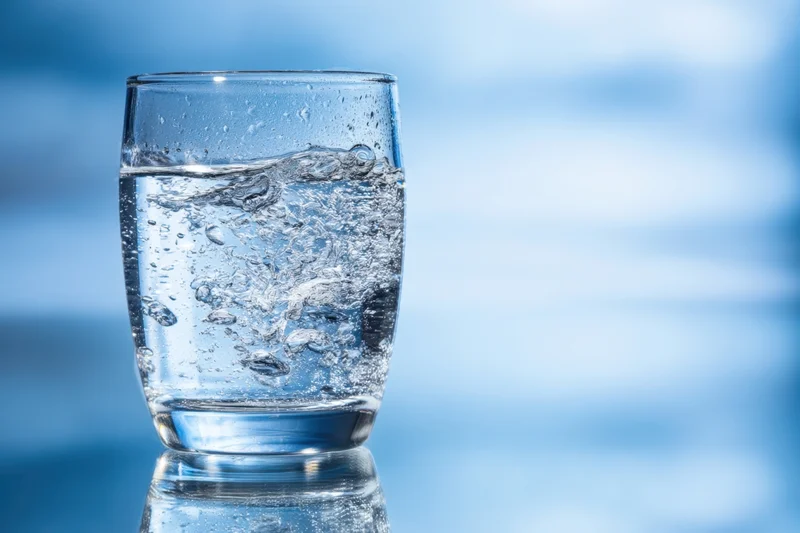 Clear glass of water with bubbles and condensation on a reflective blue surface