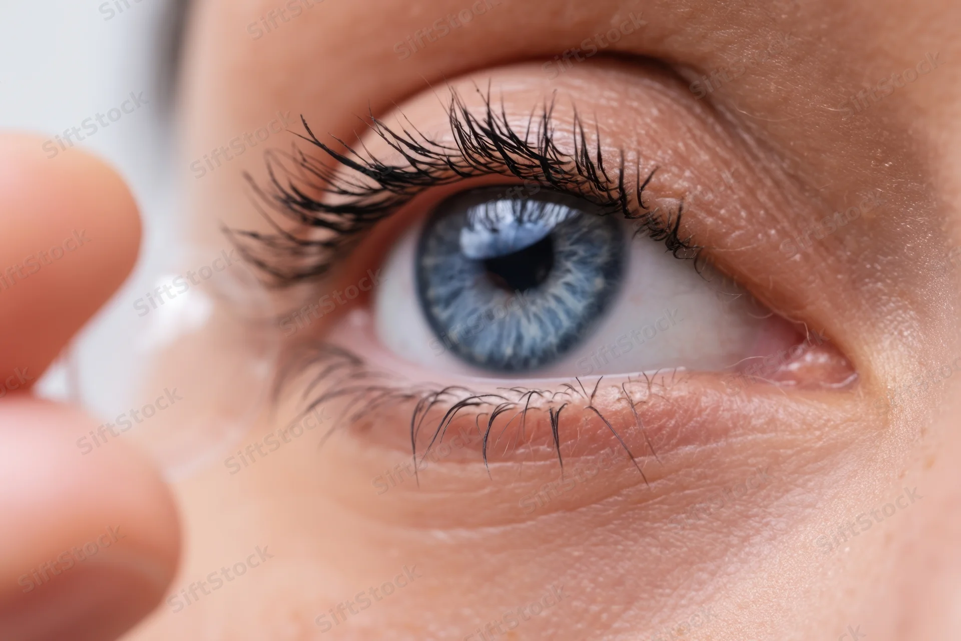 Close-up of a woman’s blue eye with a contact lens being inserted
