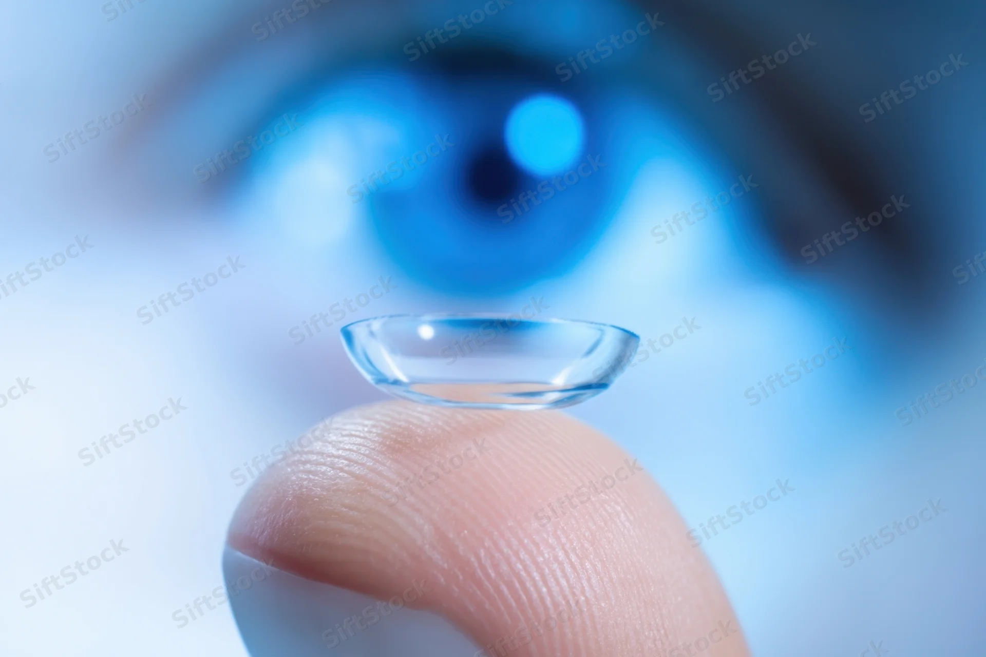 Contact lens balanced on fingertip with blurred blue eye in background
