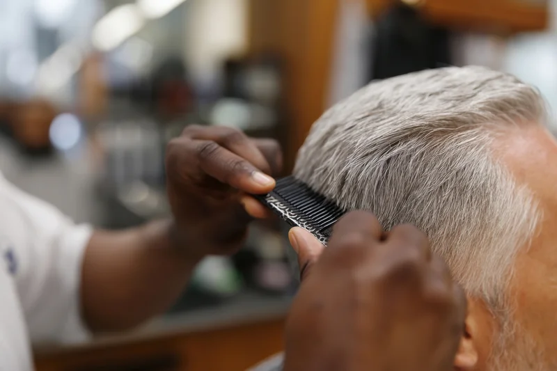 Barber combing gray hair of elderly man in salon