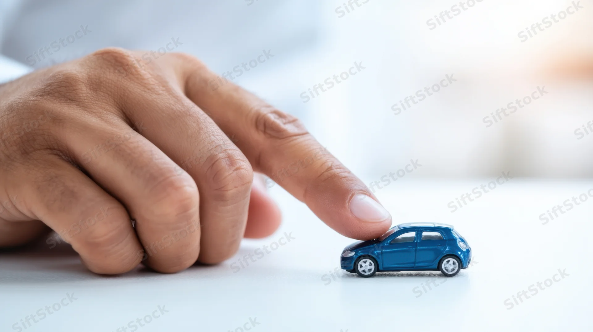 Hand touching a blue toy car on a white surface