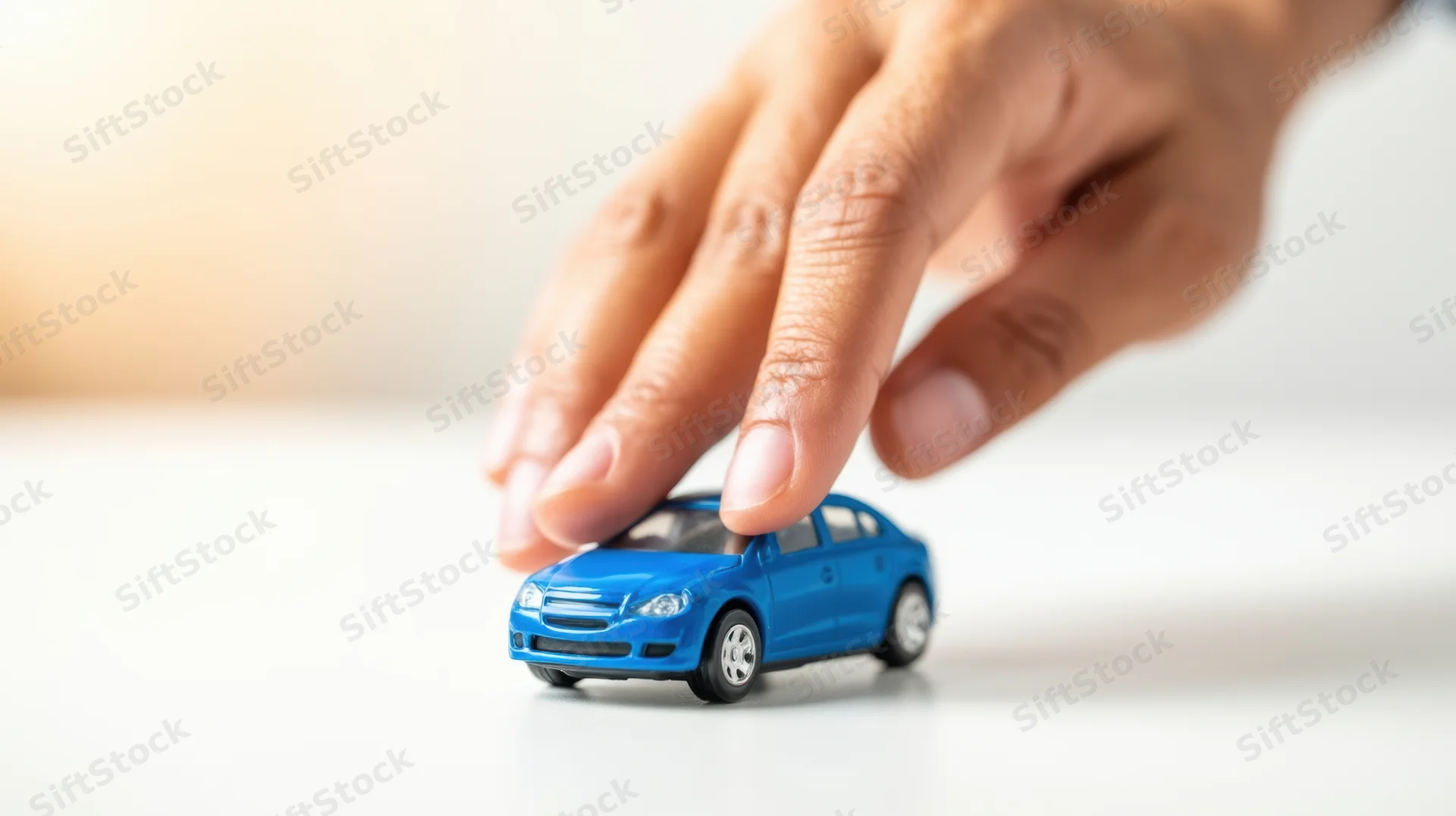 Hand touching a blue toy car on a white surface