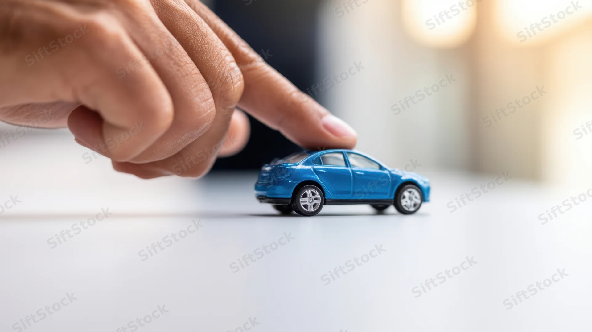 Hand pointing at a blue toy car on a white surface