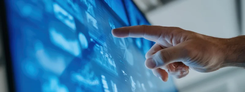 Hand touching a glowing blue digital display in an office setting