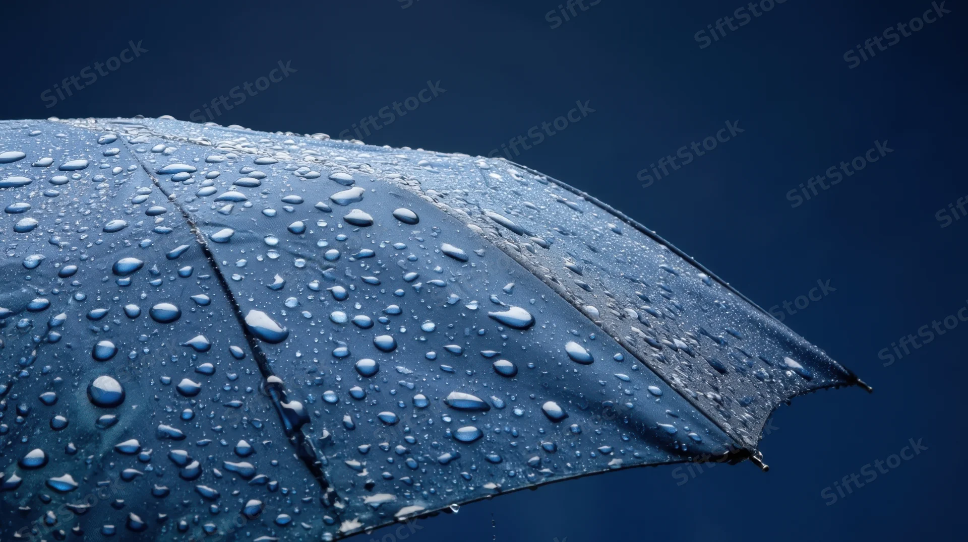 Close-up of a blue umbrella covered in raindrops against a dark sky