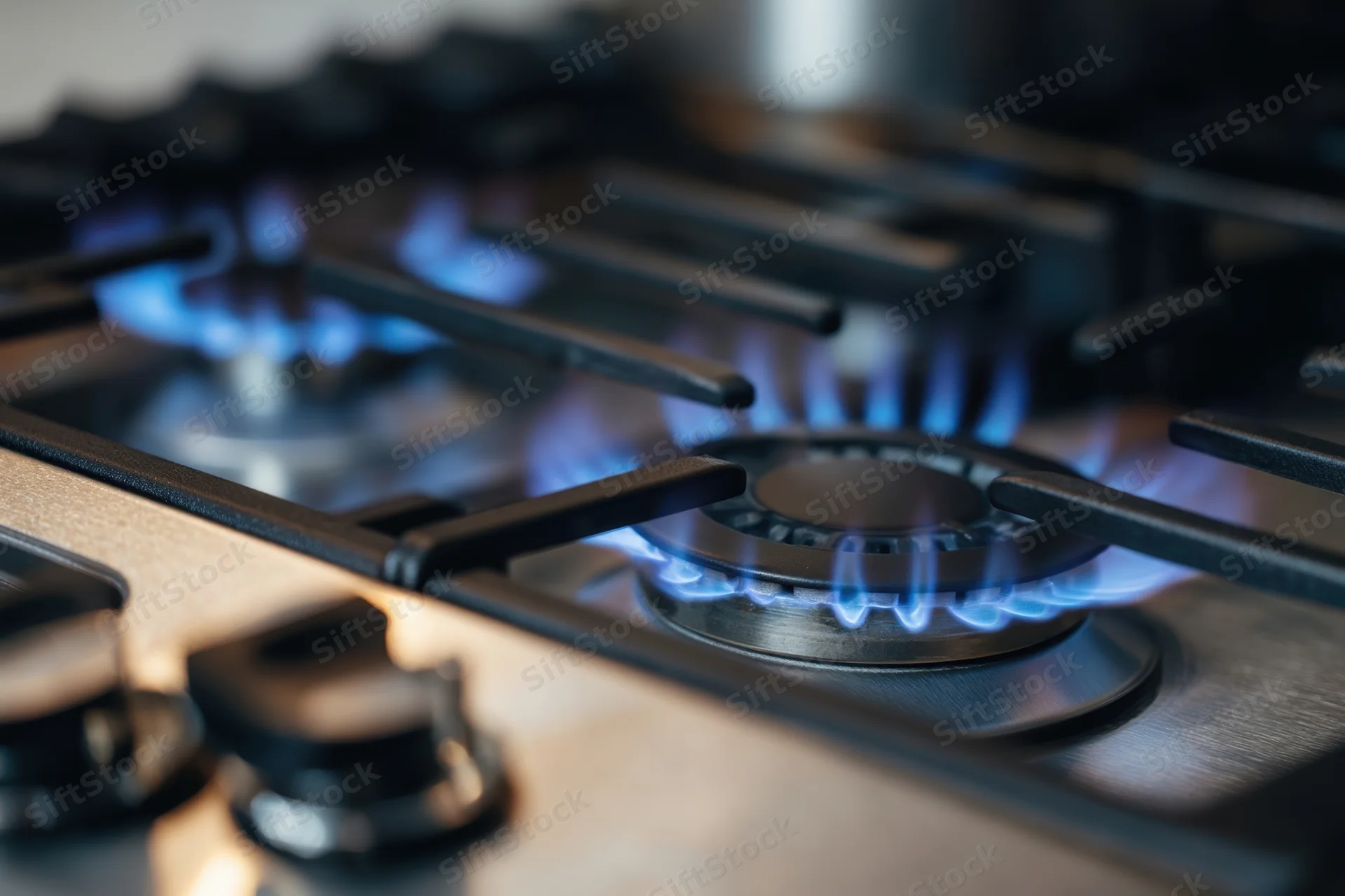 Close-up of blue flames burning on a gas stove cooktop with metal grates and control knobs
