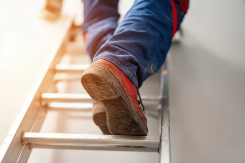 Worker's feet in red boots climbing a metal ladder indoors