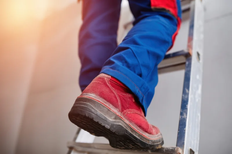 Worker climbing a ladder in work boots and blue pants