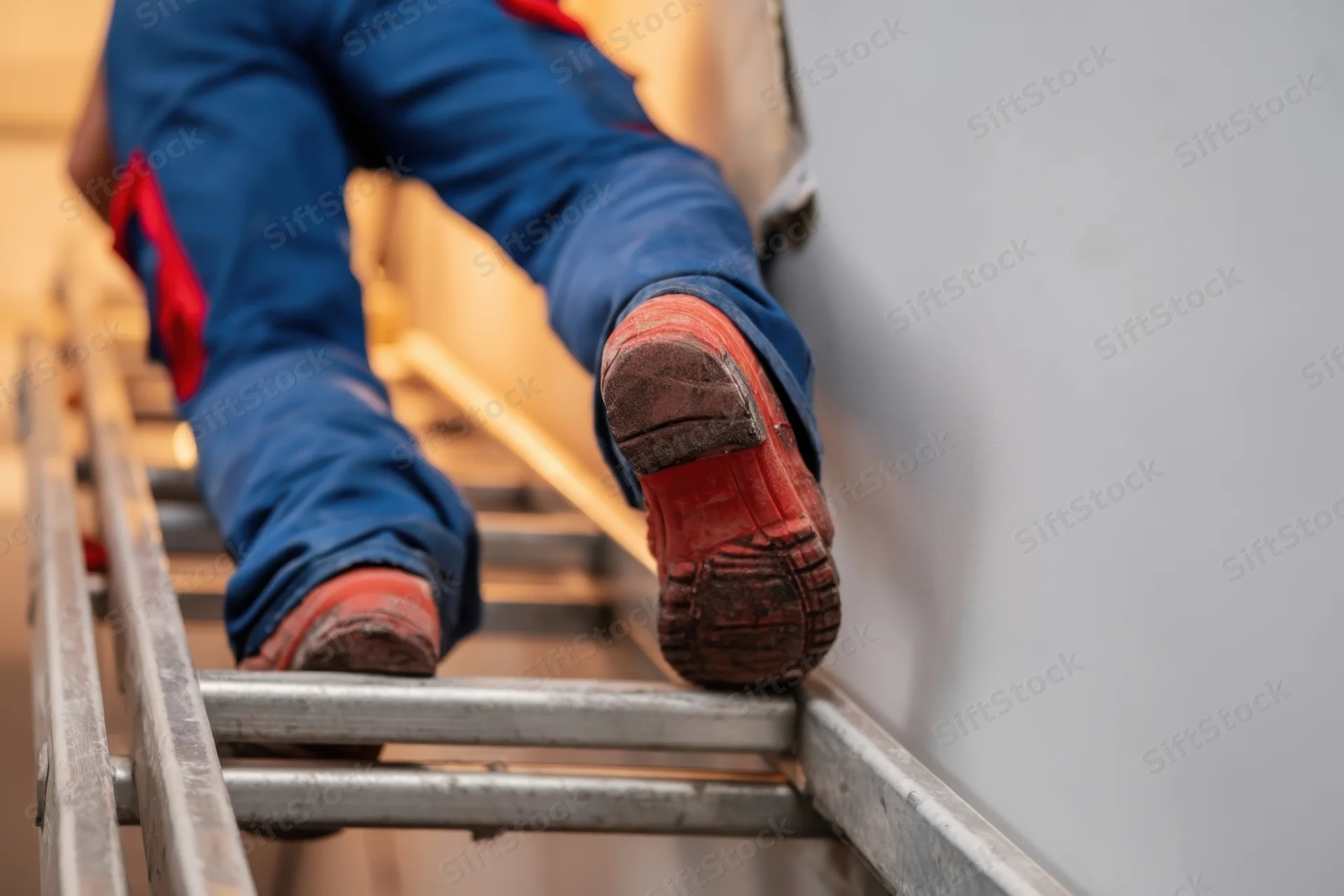 Worker climbing a metal ladder in blue workwear and red safety boots