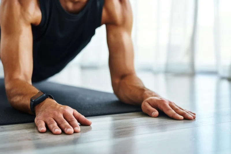 Man doing pushup on exercise mat indoors with smartwatch on wrist
