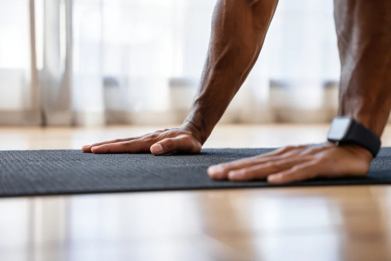 Man doing pushup on exercise mat indoors with smartwatch on wrist