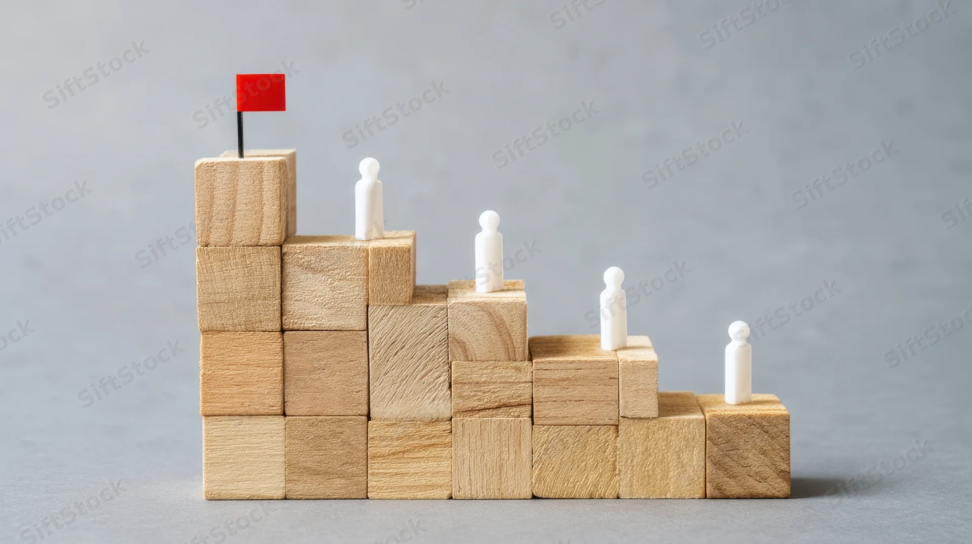 Wooden blocks arranged in ascending steps with white figures and a red flag on top symbolizing career progression