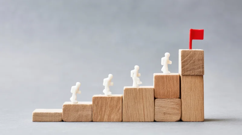Miniature figures climbing wooden blocks toward a red flag at the top