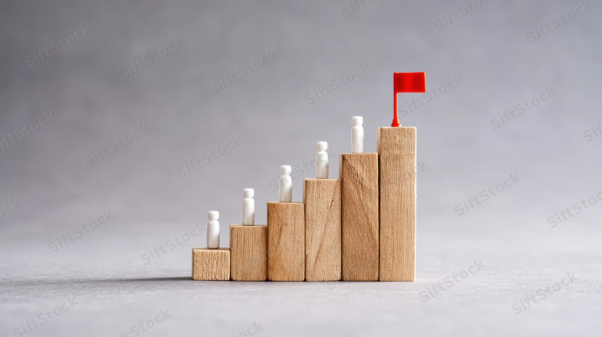 Wooden blocks arranged in ascending order with small white figures and a red flag on top, symbolizing growth and achievement in business