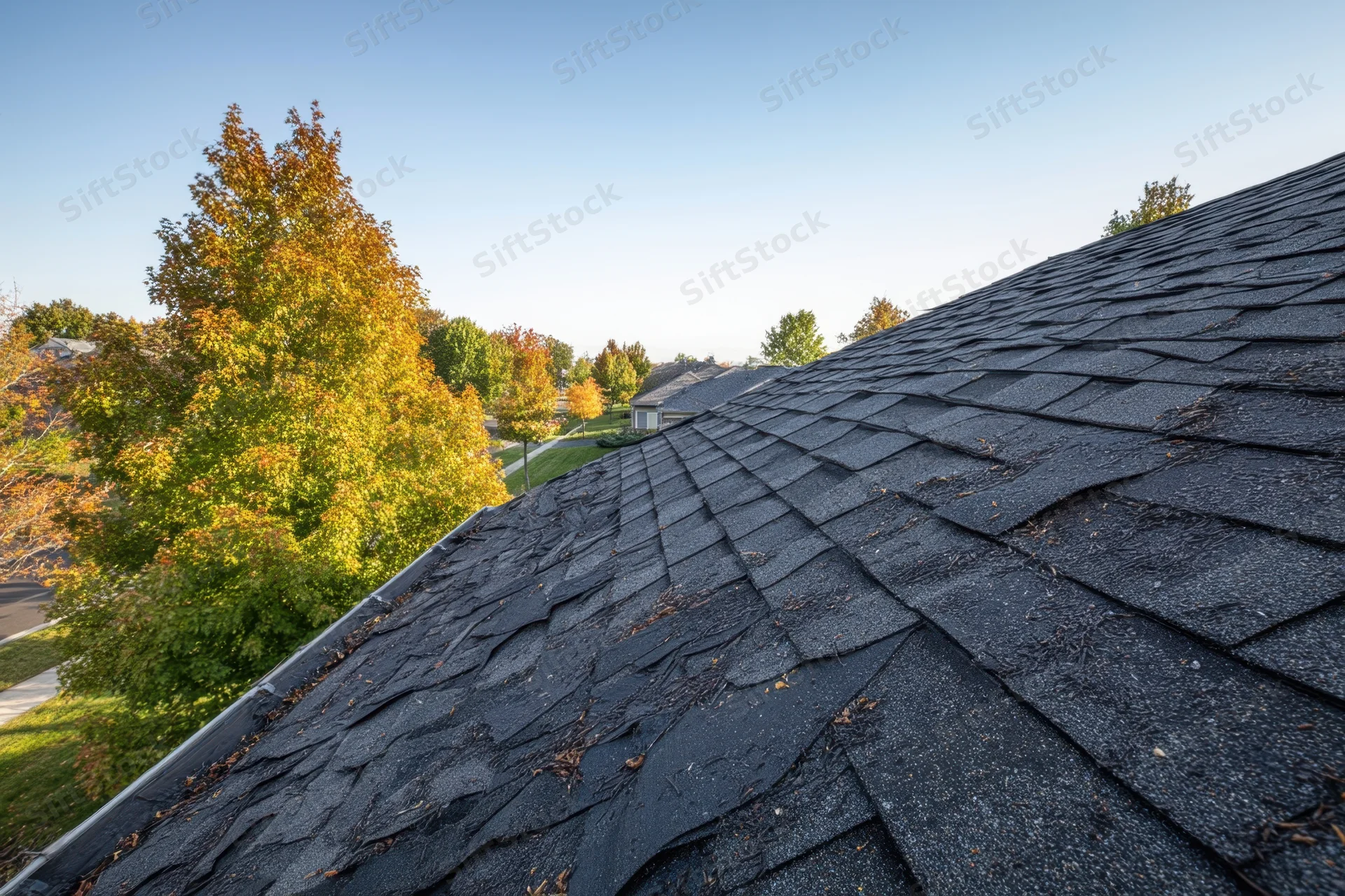 Damaged asphalt shingle roof on a residential home with autumn trees in the background