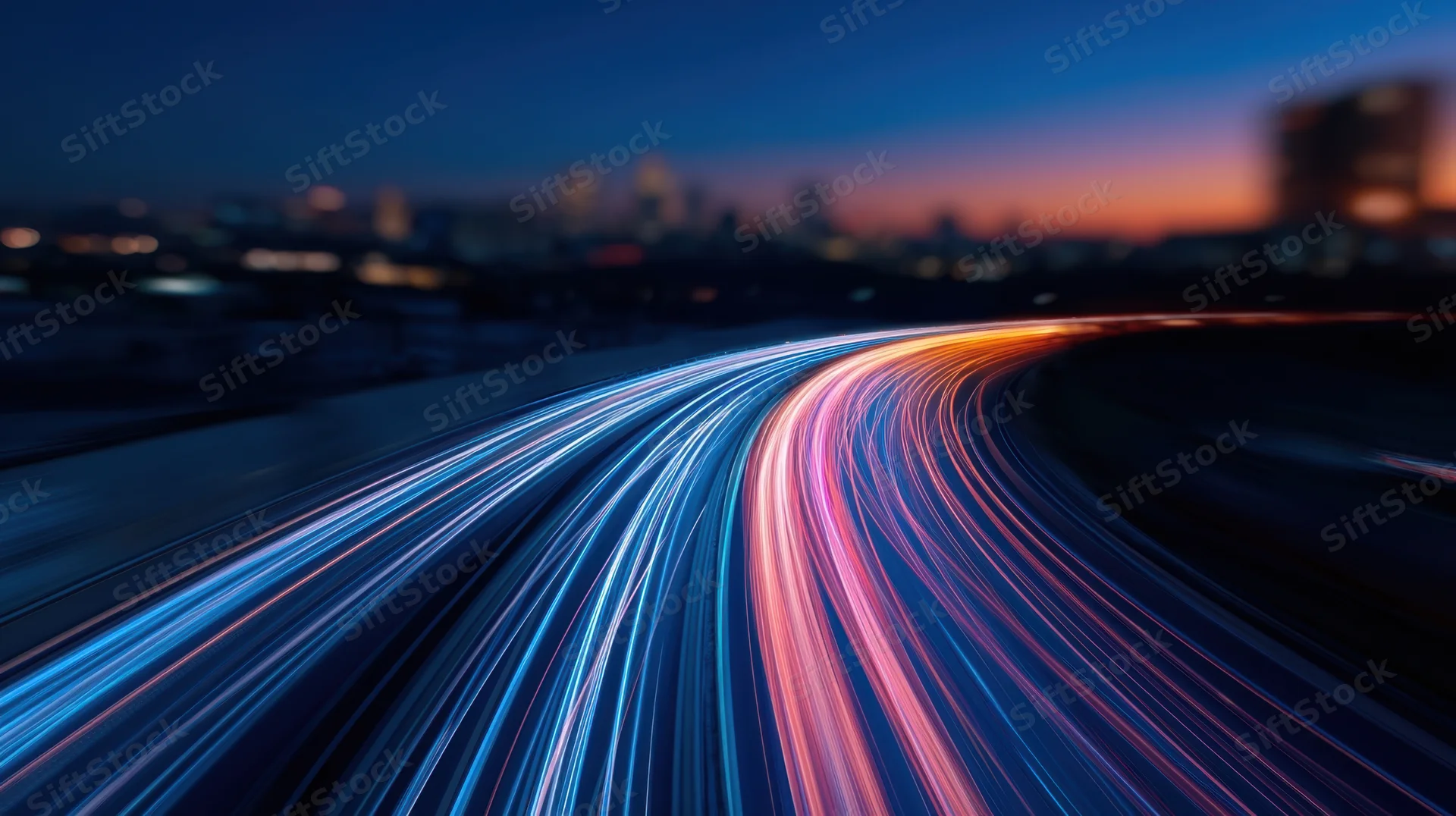 Light trails from moving vehicles on a curving highway at night with city skyline in background