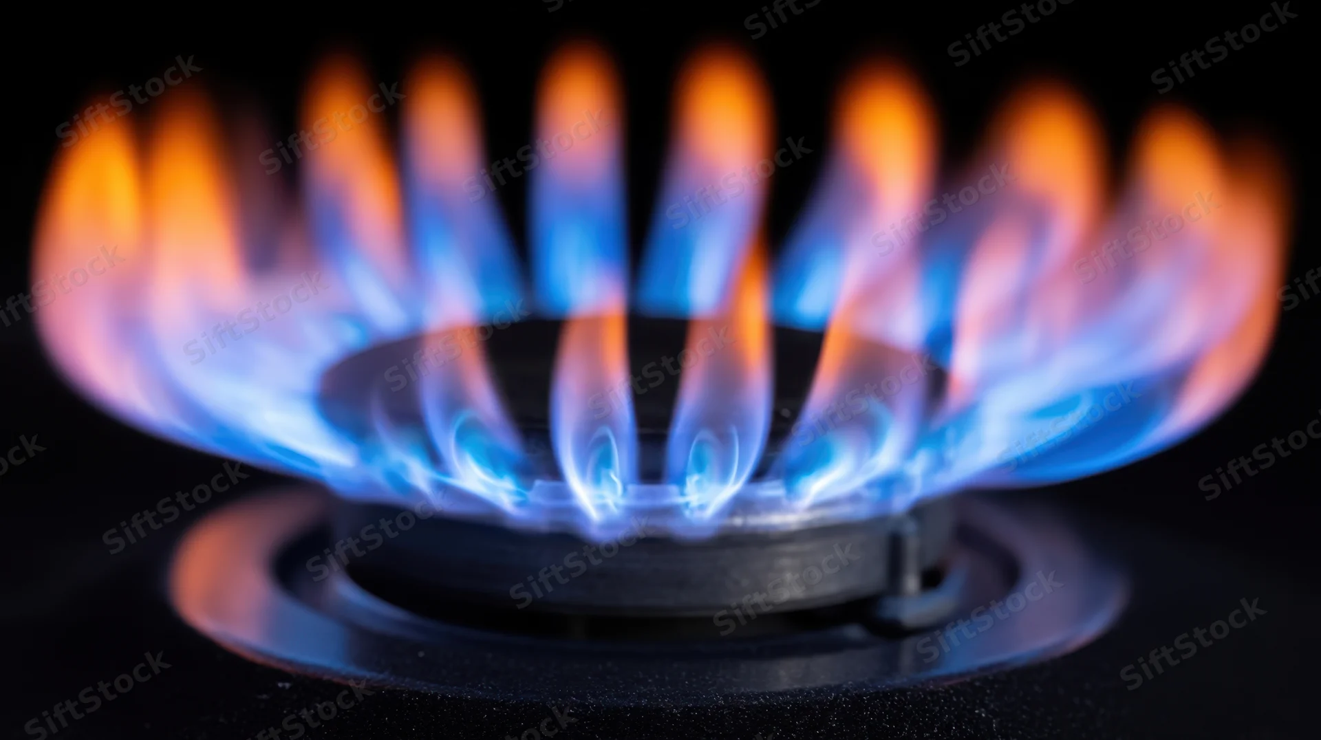 Blue and orange flame burning on a gas stove burner in a dark kitchen setting