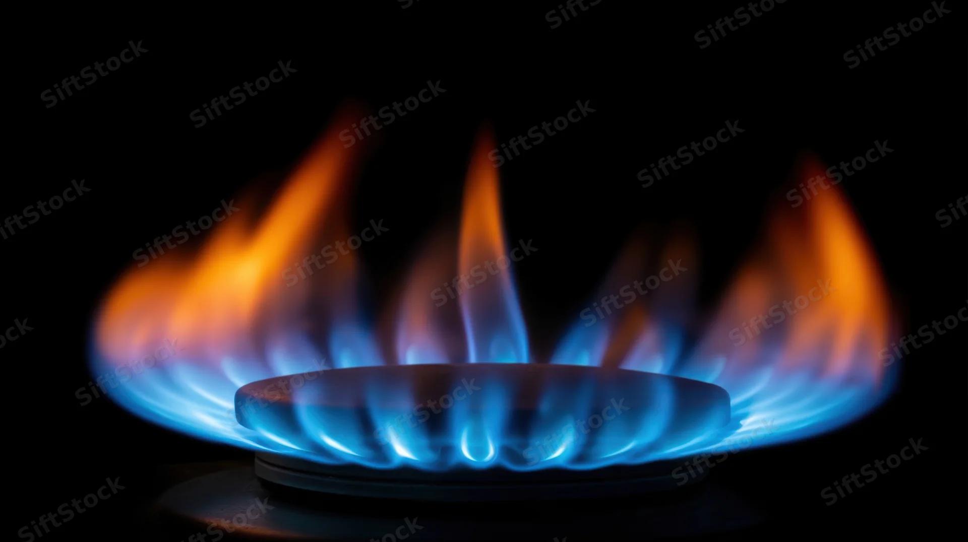 Blue and orange flame burning from a gas stove burner against a dark background