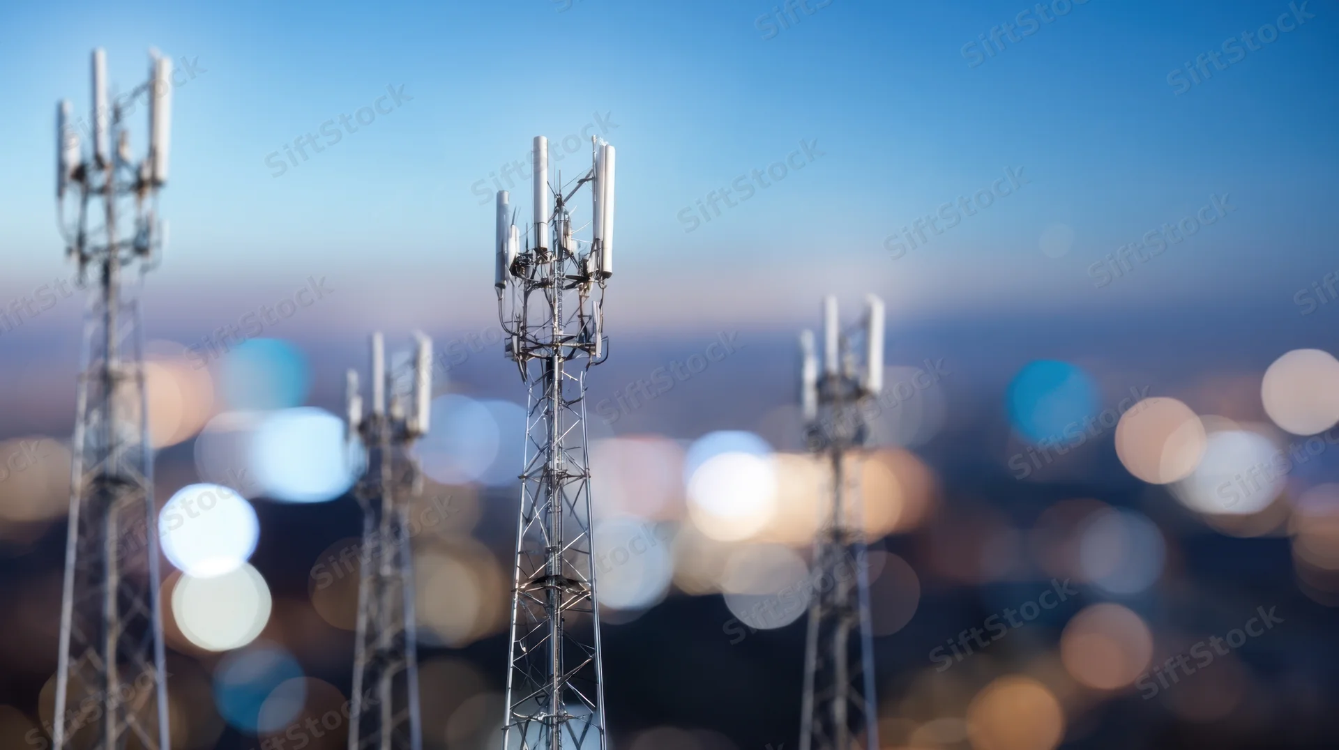 Communication towers with antennas against a blurred city skyline at night