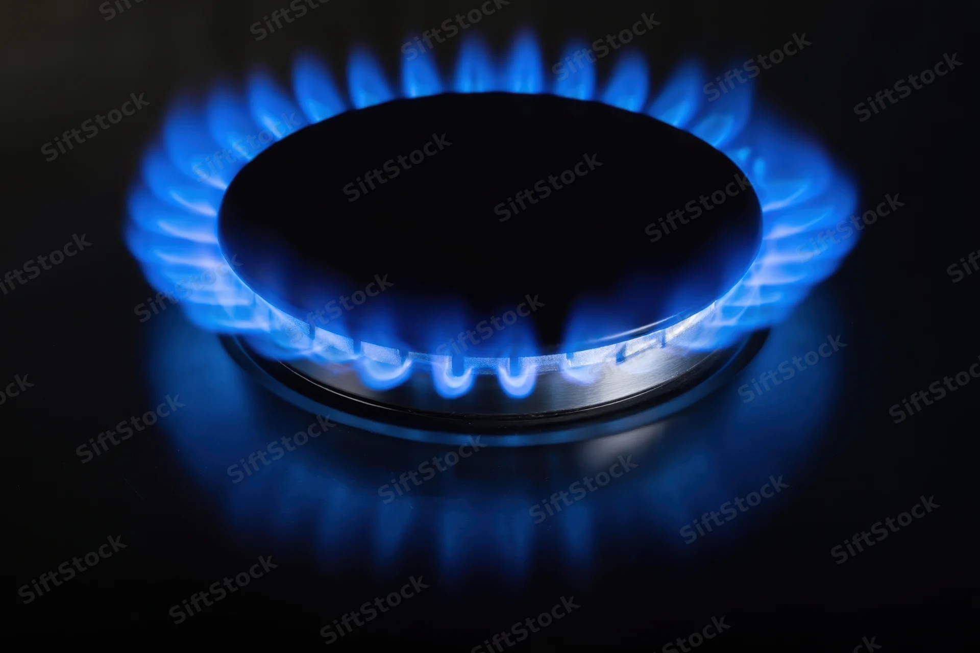 Blue flame burning on a gas stove burner in a dark kitchen setting