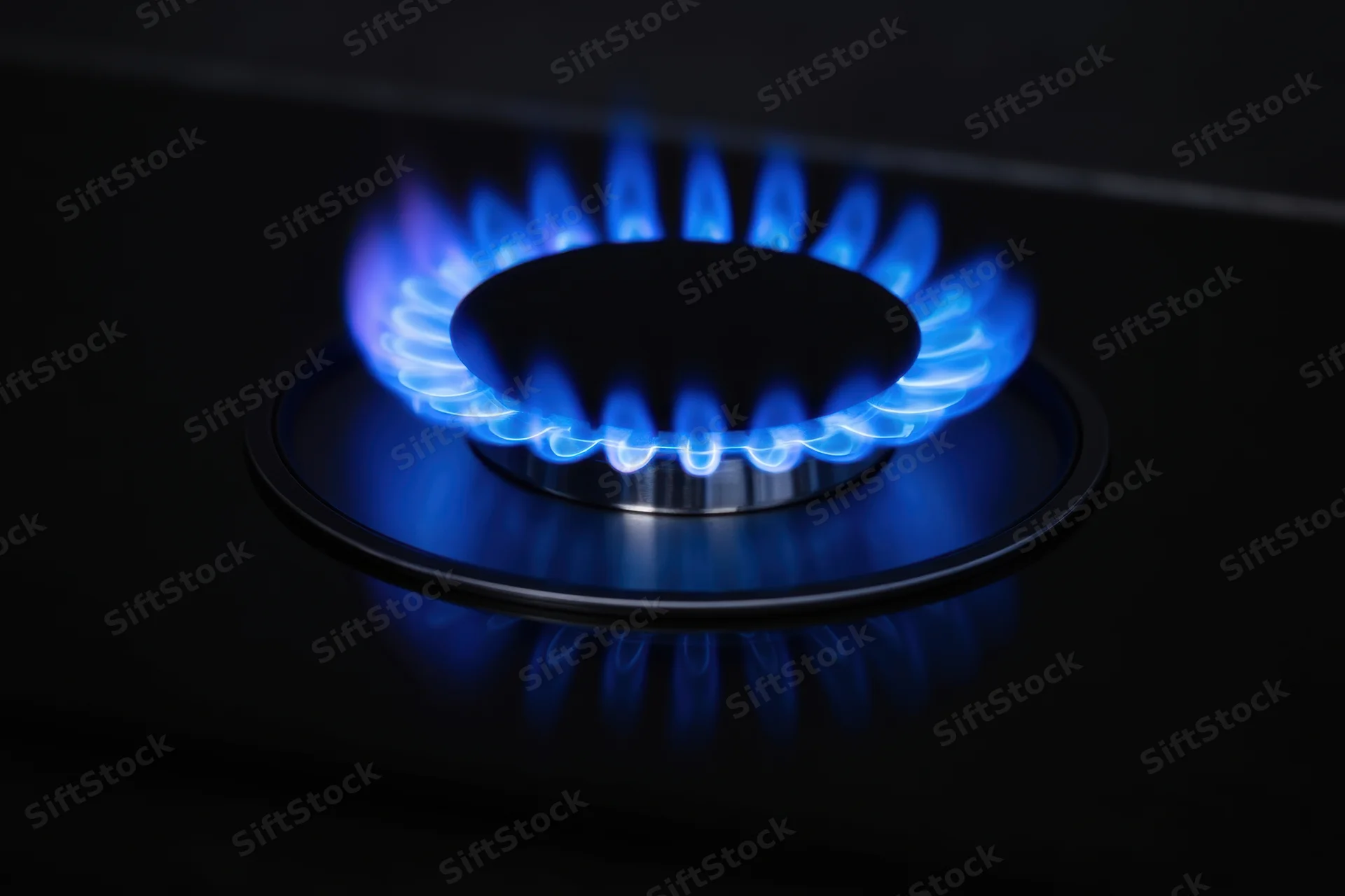 Blue flame burning on a gas stove burner in a dark kitchen setting