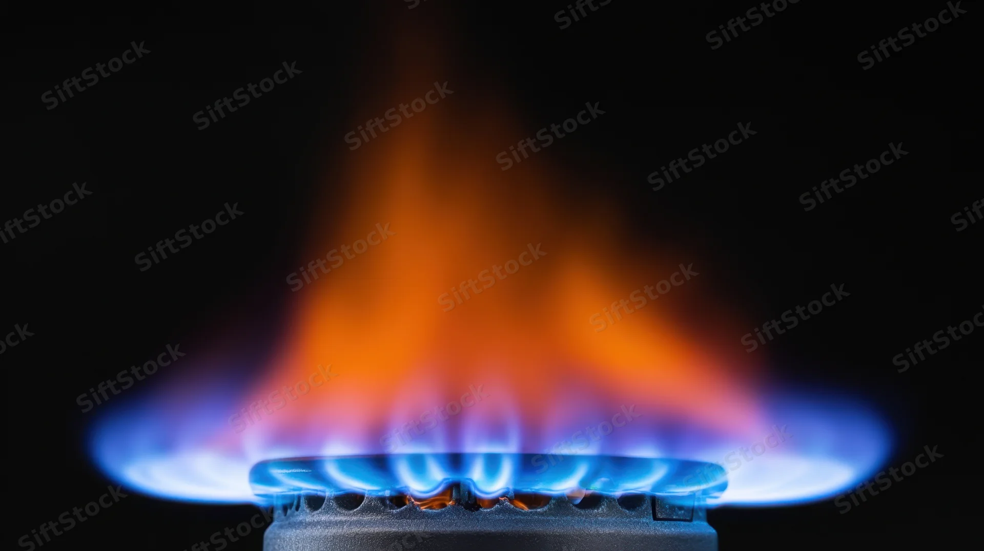 Blue and orange flame burning from a gas stove burner against black background