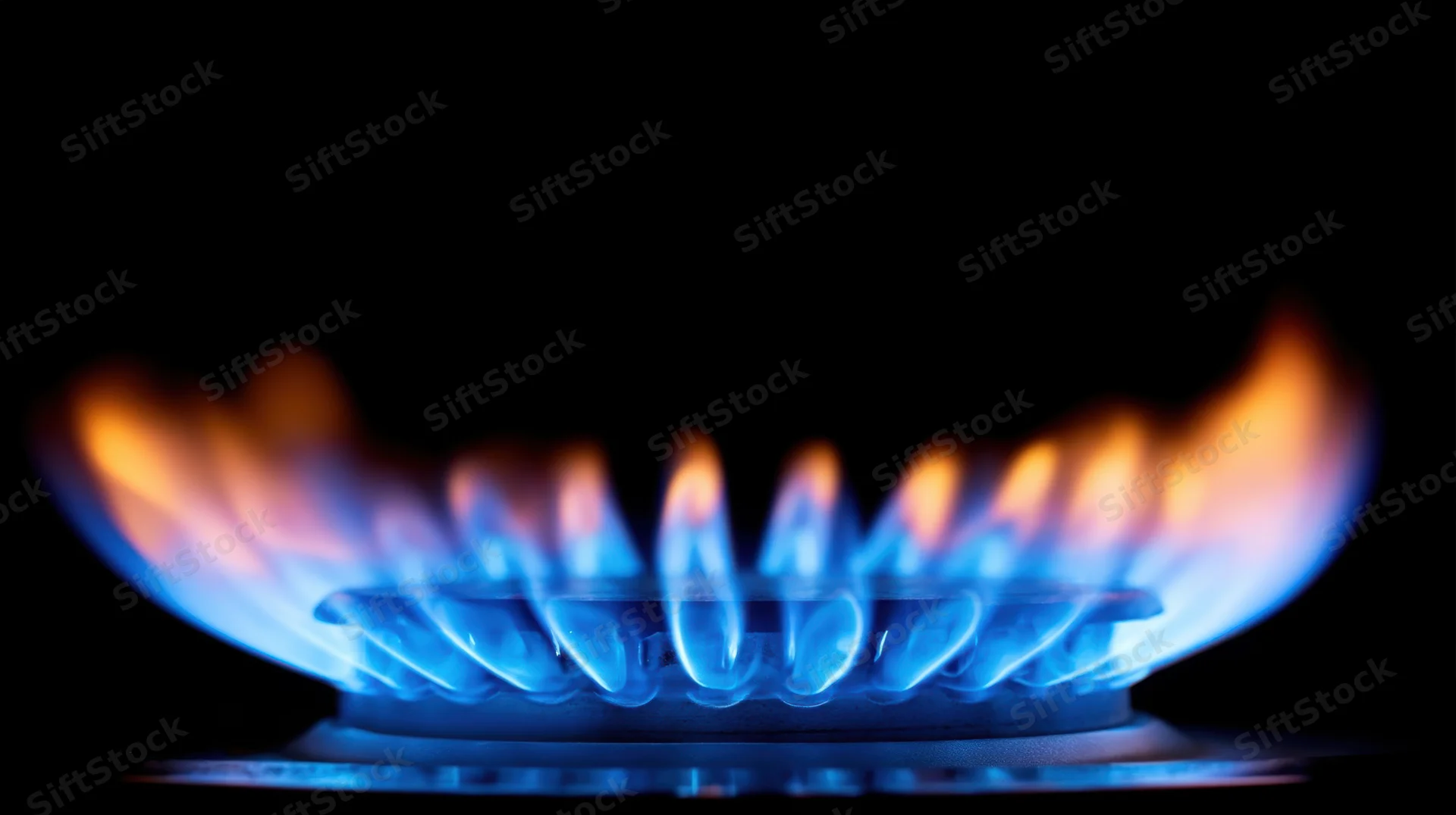 Blue flame burning on a gas stove burner in a dark kitchen setting