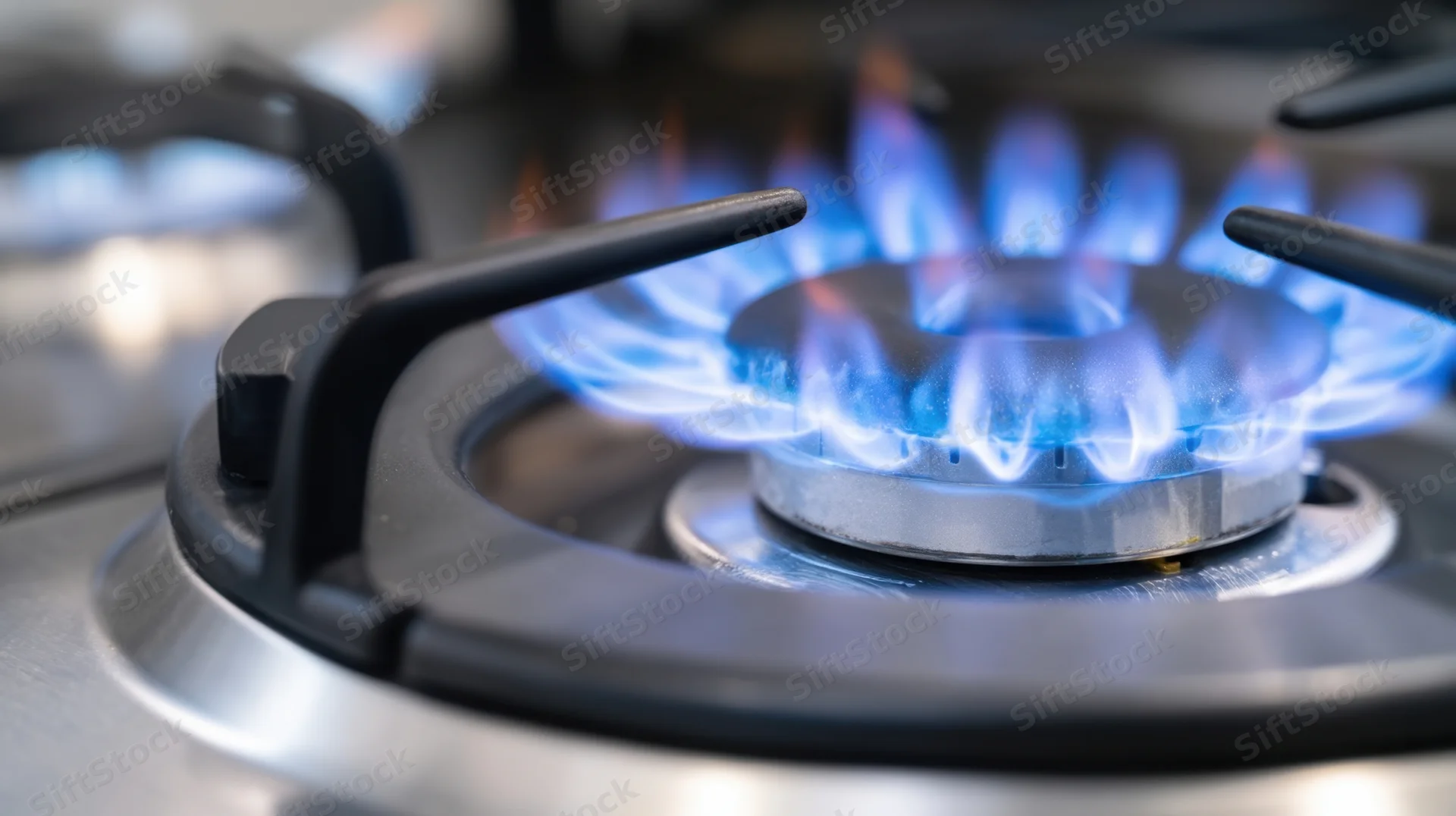 Close-up of a gas stove burner with blue flame ignited on a stainless steel cooktop
