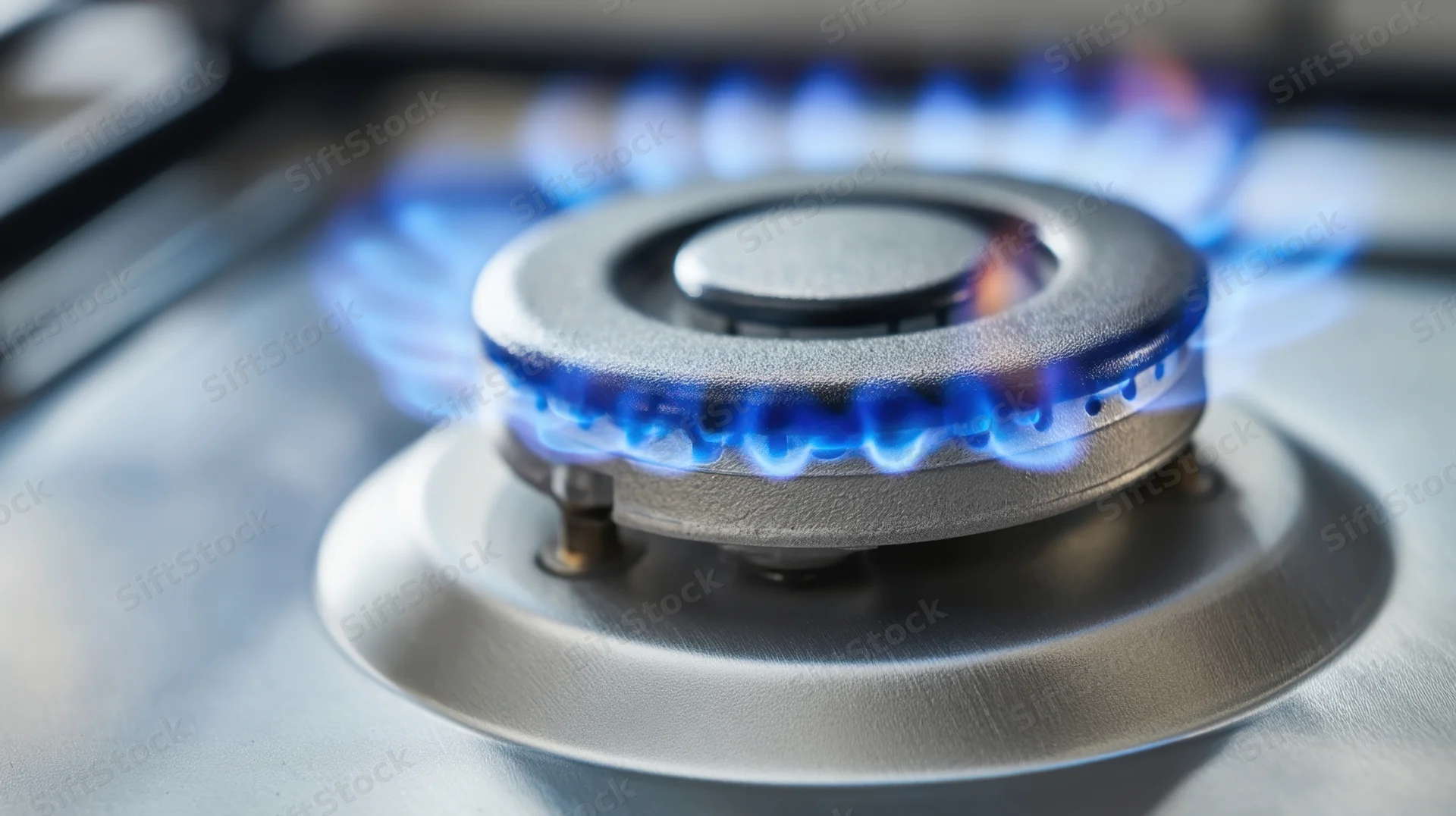 Close-up of a gas stove burner with blue flame on a stainless steel cooktop