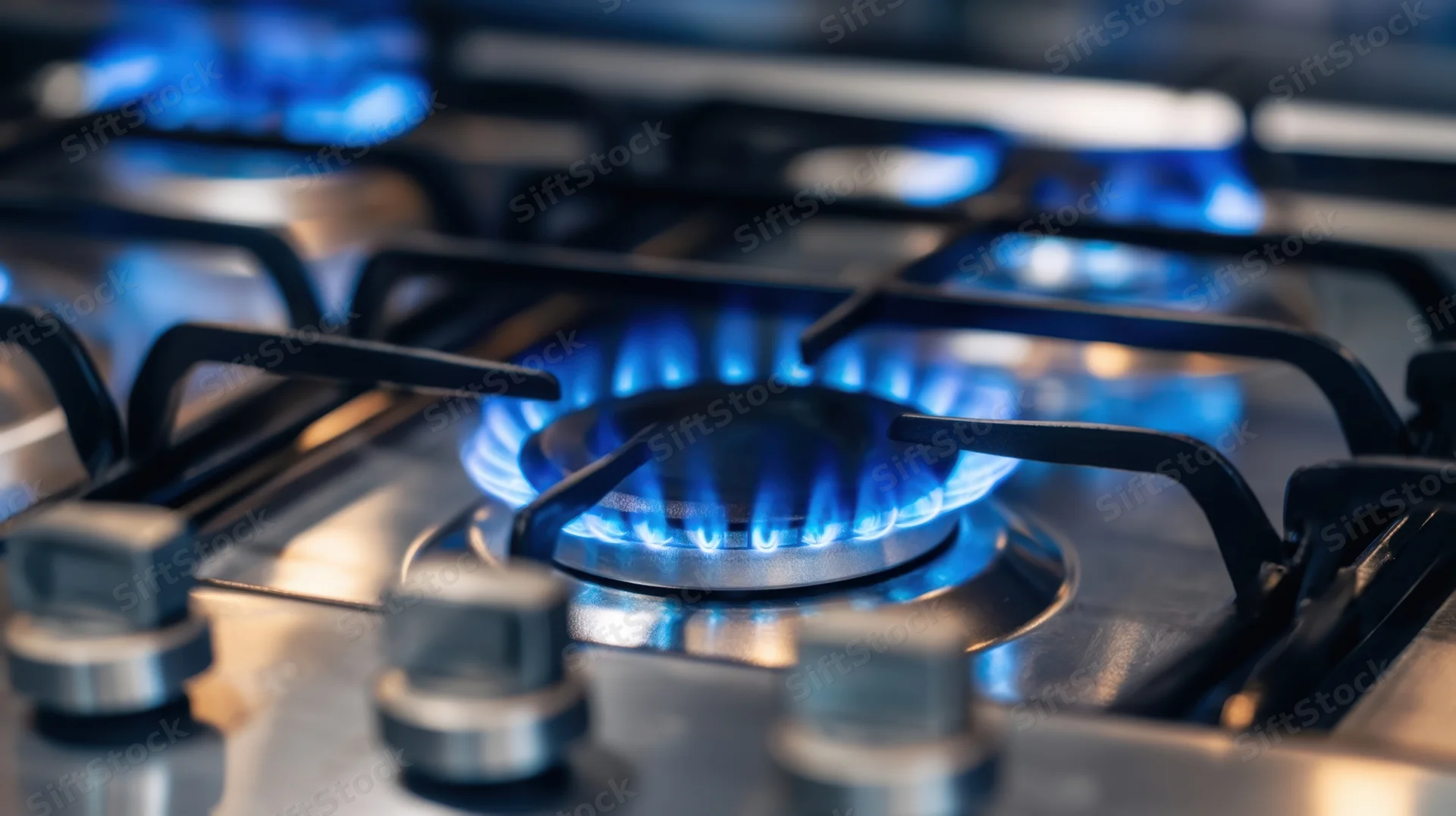 Close-up of blue flames burning on a stainless steel gas stove cooktop