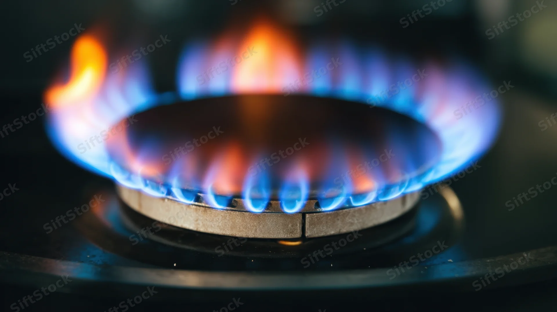 Close-up of a lit gas stove burner with blue and orange flames on a kitchen cooktop
