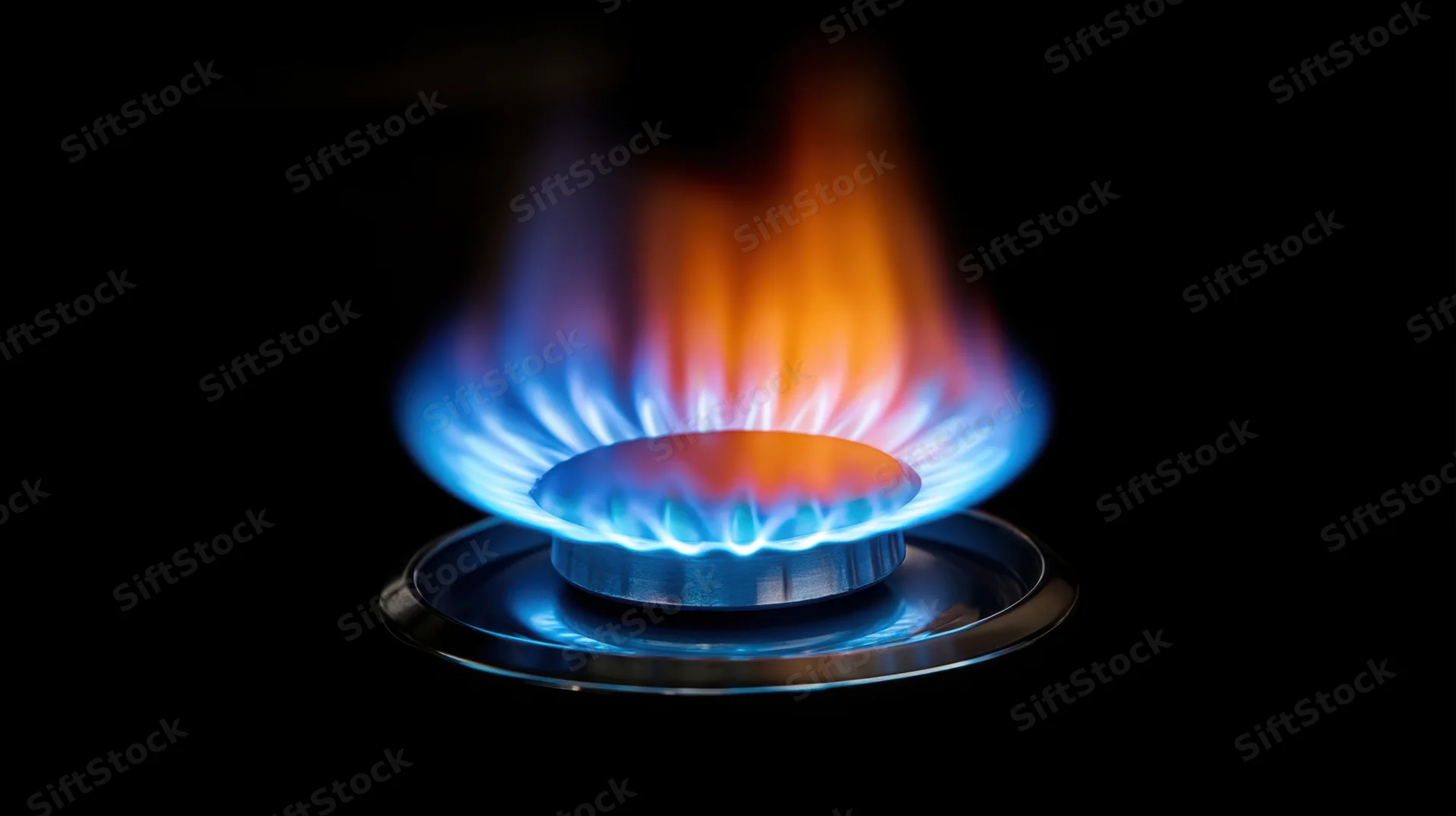 Gas stove burner with blue and orange flame against black background