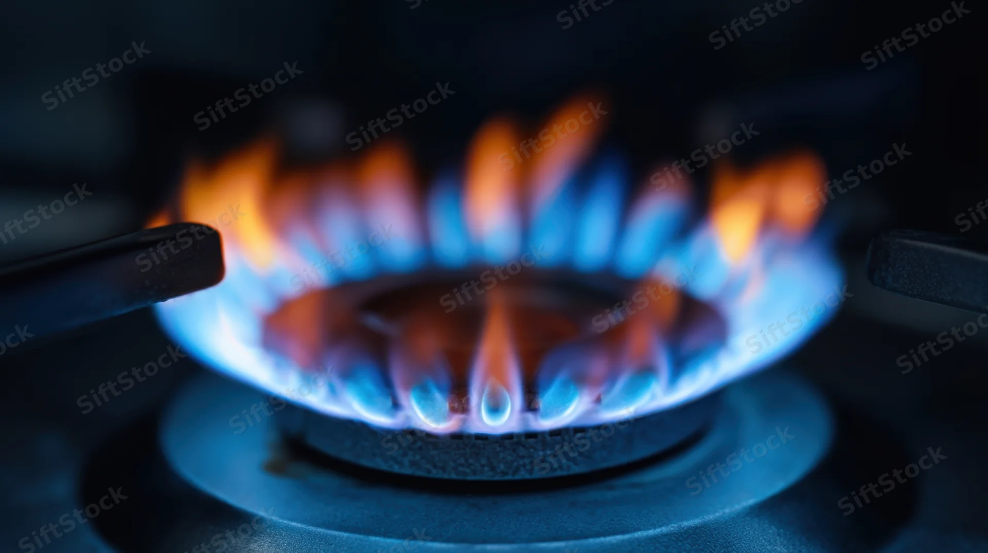 Blue and orange flames burning on a gas stove burner in a kitchen setting