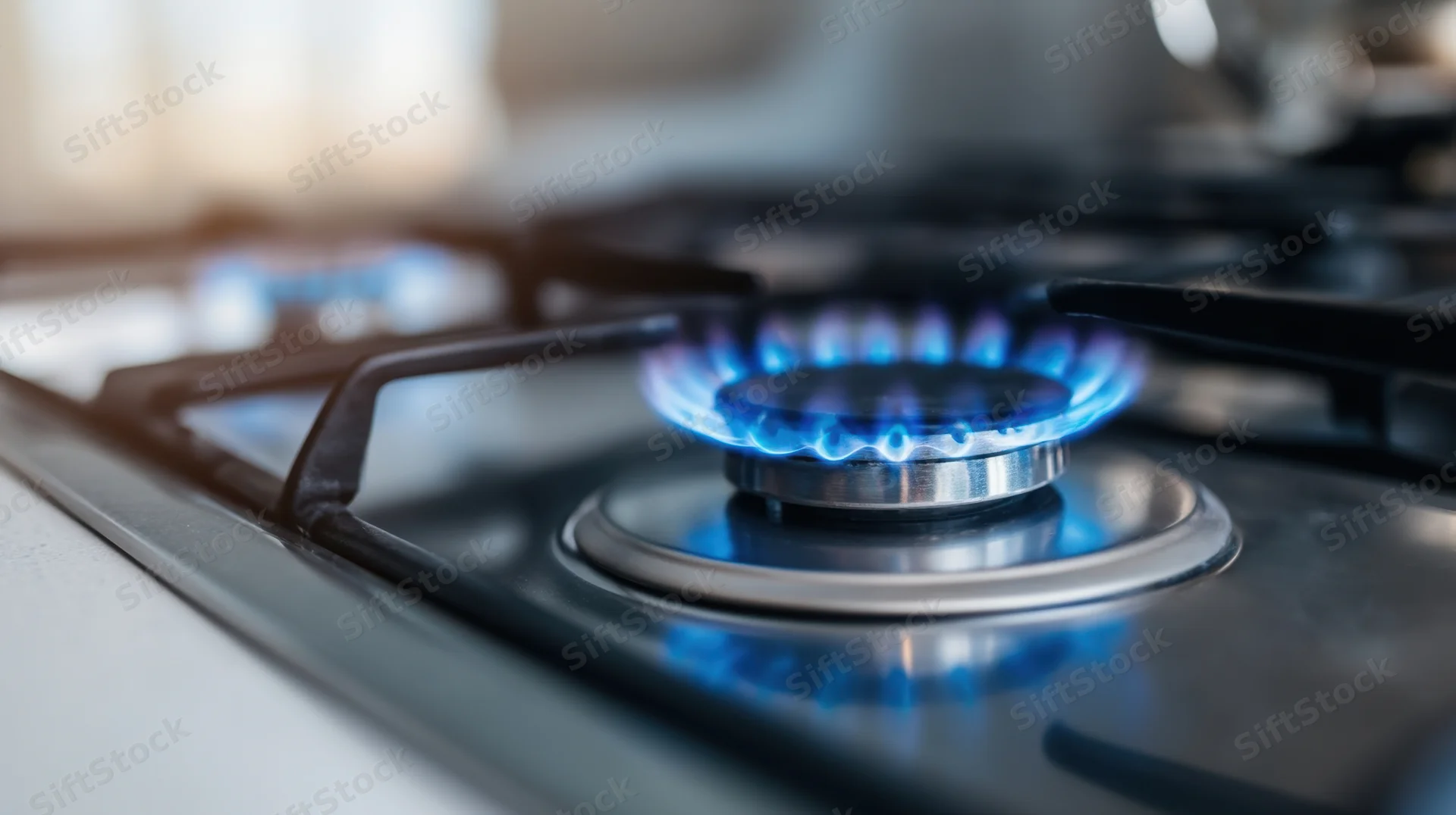 Close-up of a lit gas stove burner with blue flame on a stainless steel cooktop