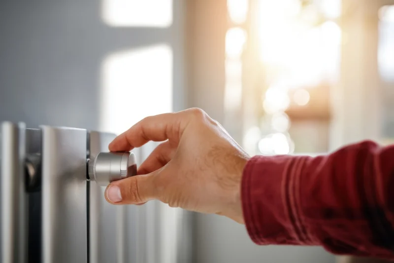 Hand adjusting a radiator knob for temperature control in a home interior