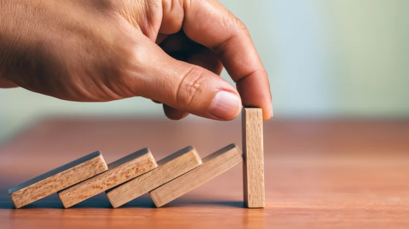 Hand stopping falling wooden dominoes on a desk