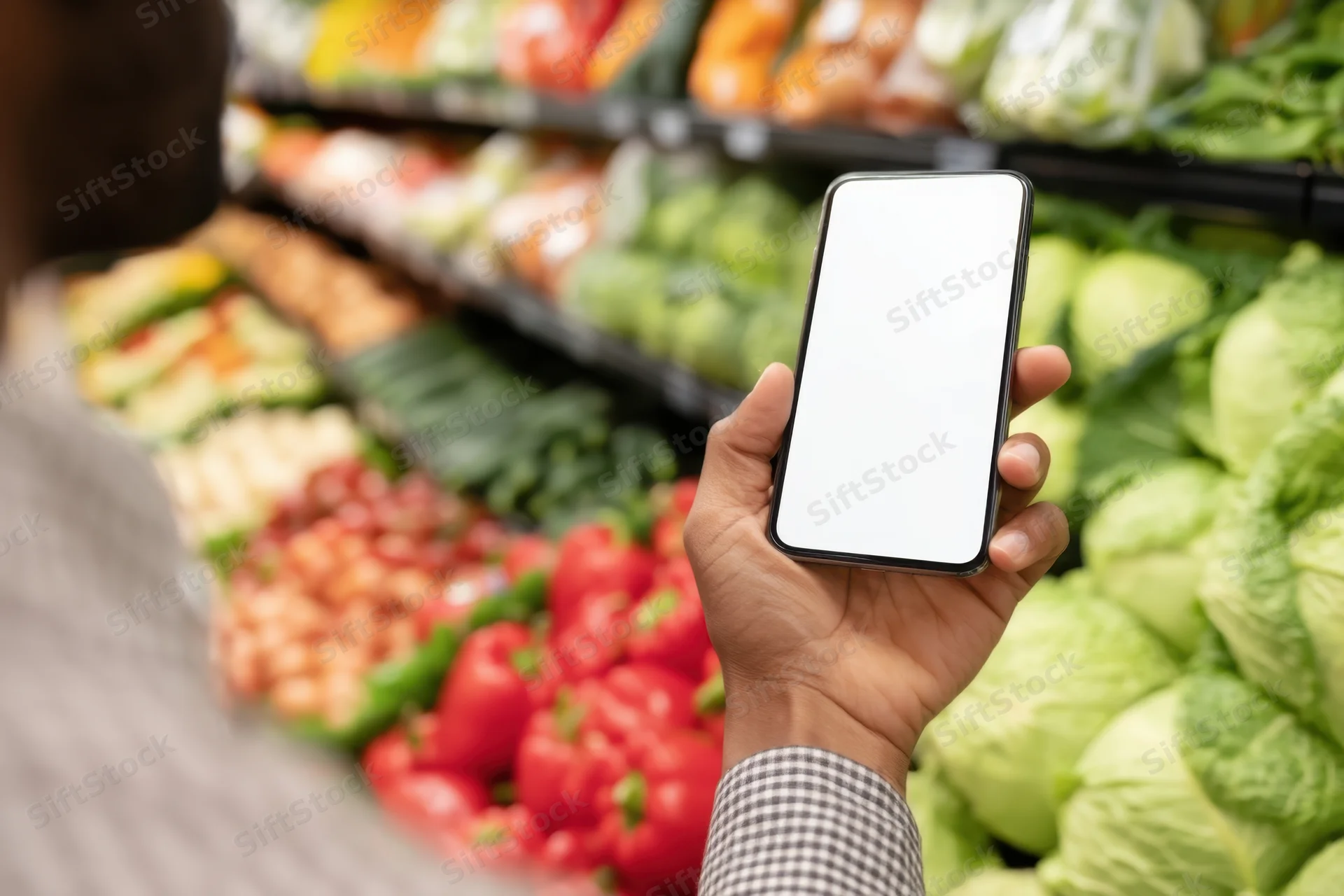 Hand holding smartphone with blank screen in grocery store produce aisle