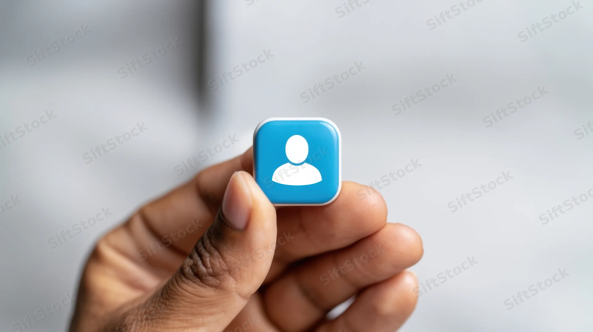 Hand holding a blue user profile icon against a blurred background