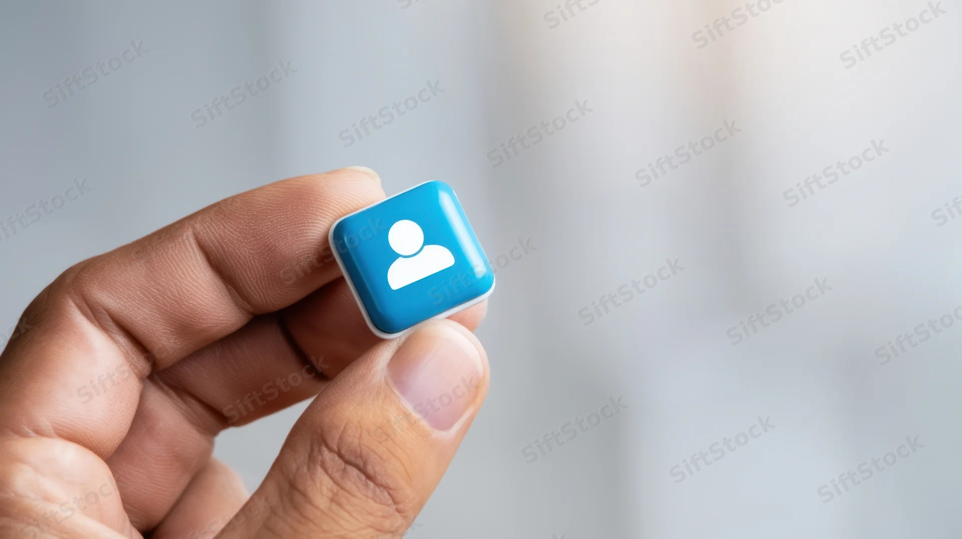 Hand holding a blue user profile icon against a blurred background
