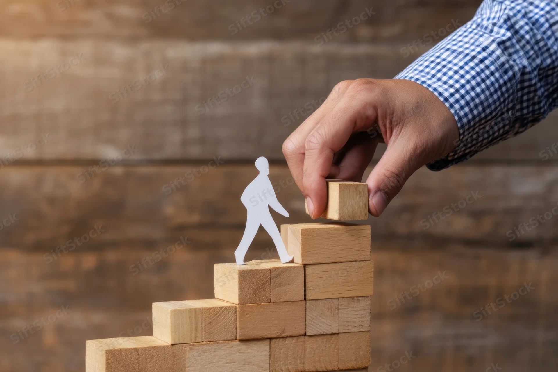 Hand placing wooden block to extend staircase for paper cutout figure climbing