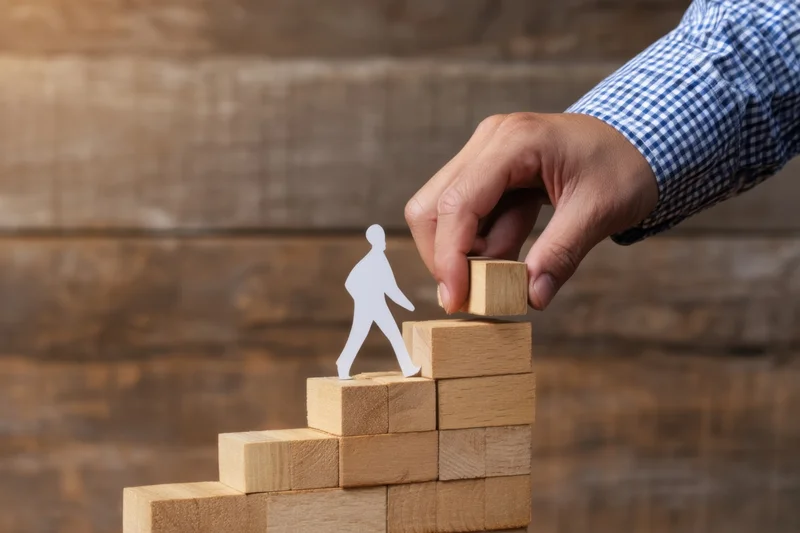 Hand placing wooden block to extend staircase for paper cutout figure climbing