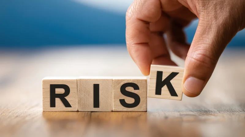 Hand placing wooden block with letter k to complete word risk on wooden surface