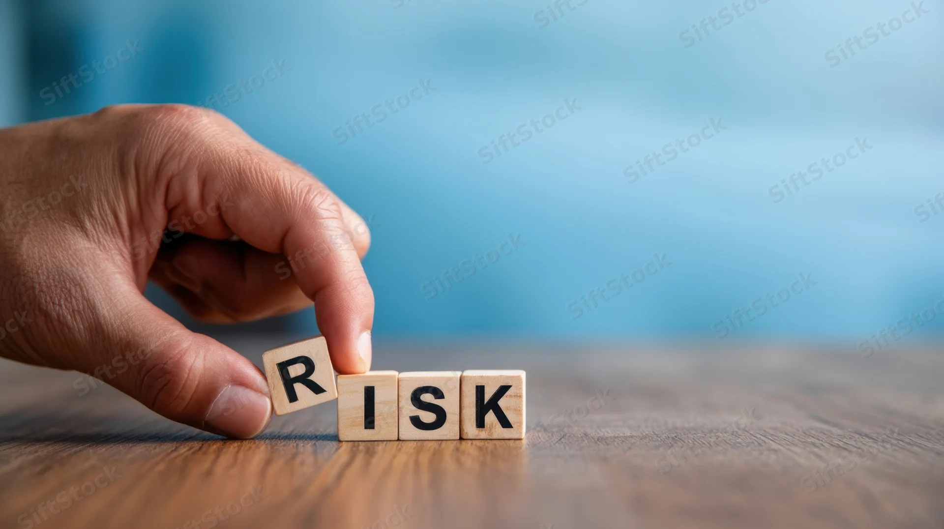 Hand placing wooden blocks spelling risk on a wooden table
