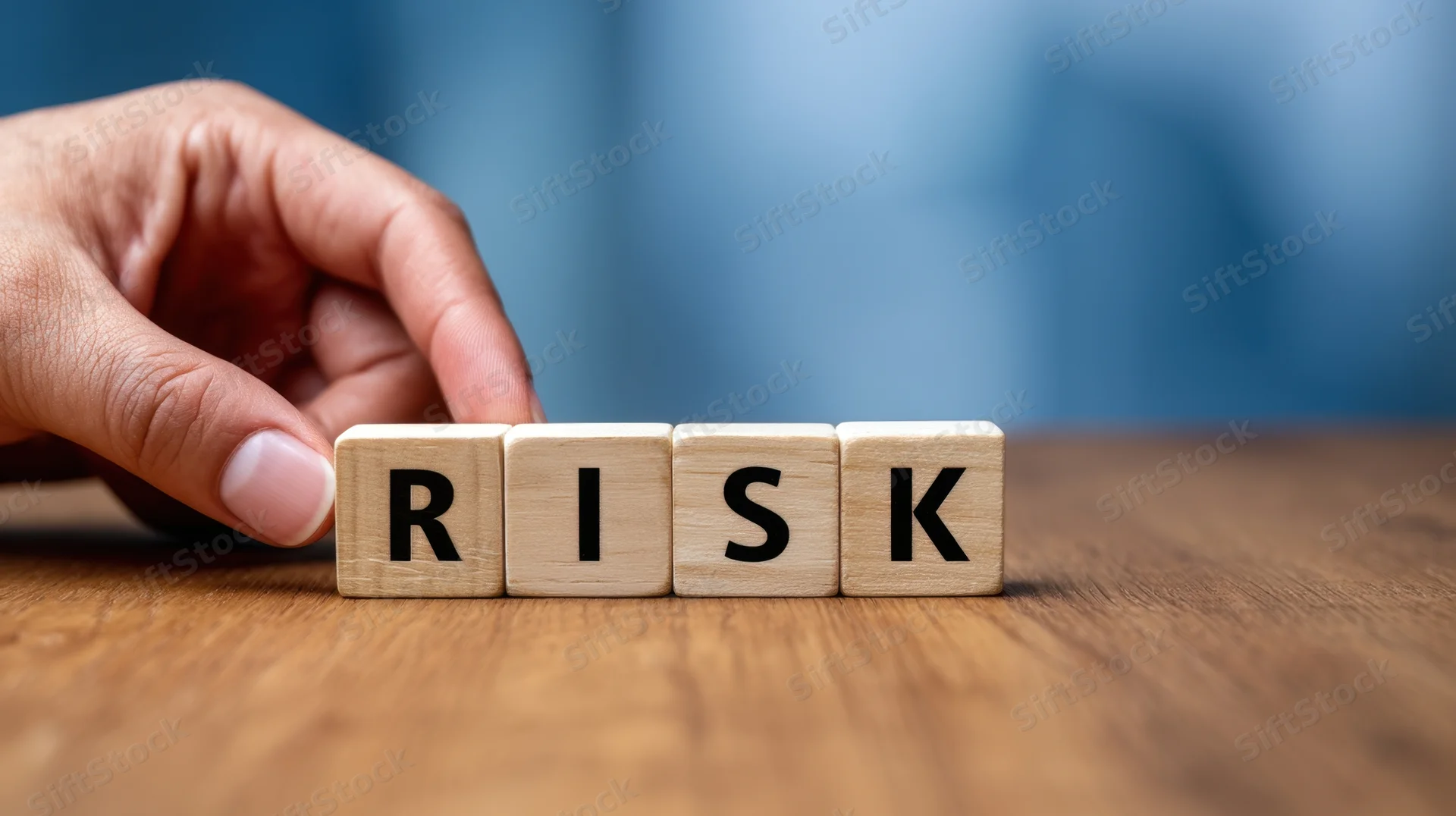 Hand arranging wooden blocks spelling risk on a wooden table